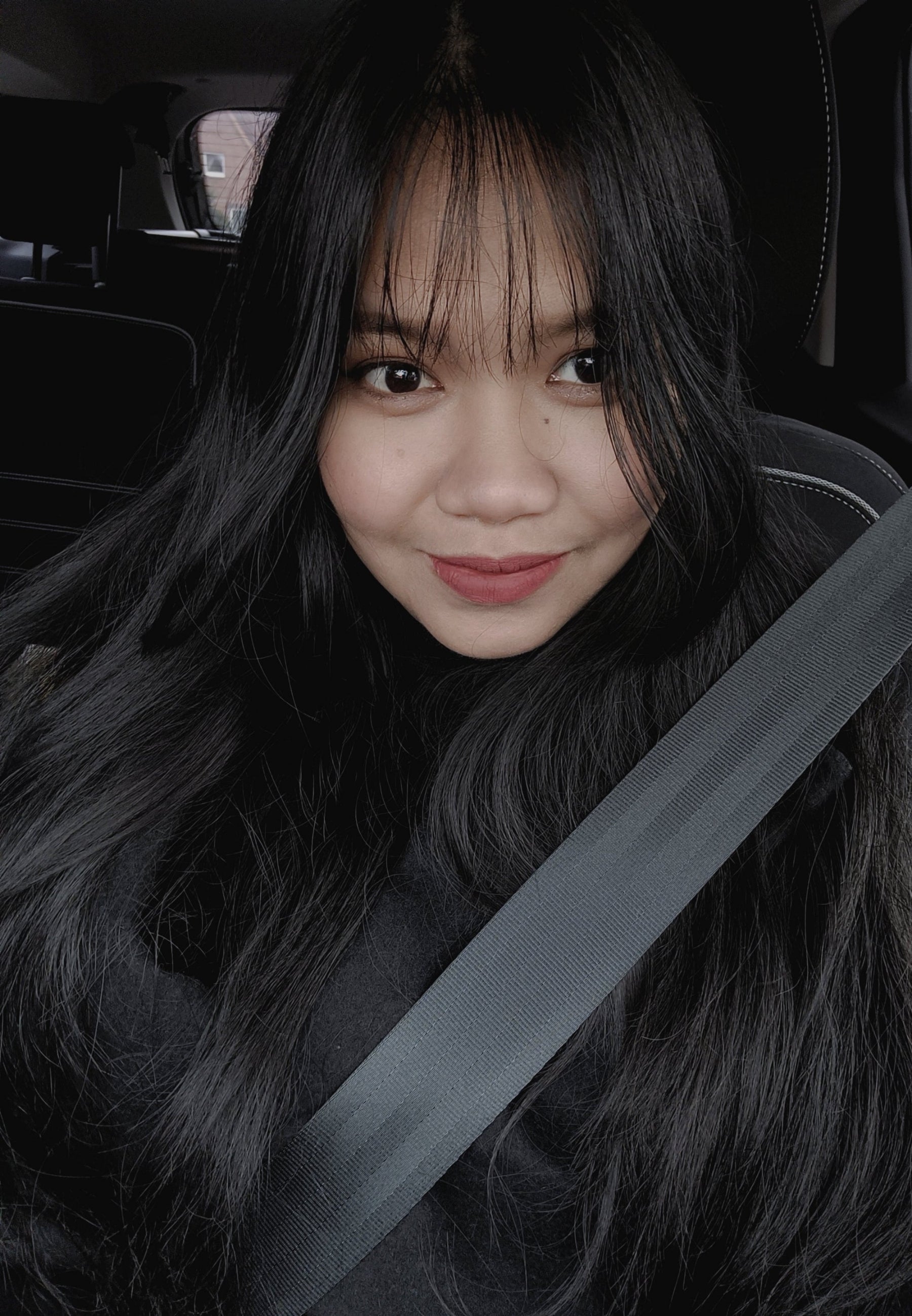 Person sitting in a car with a seatbelt on, looking at the camera.